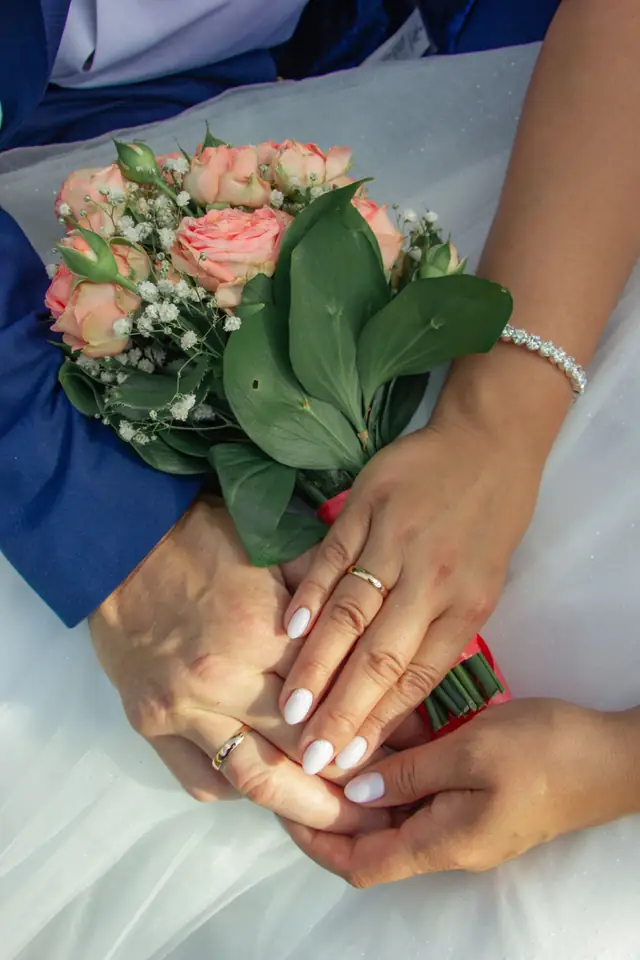 A couple's hands with wedding rings over a bouquet of roses